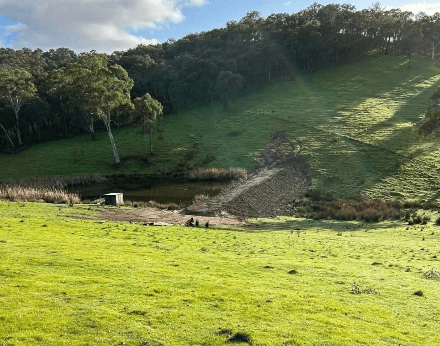 Farm dam embankment and earthworks on a green hillside - Anderson & Sons dam construction Victoria